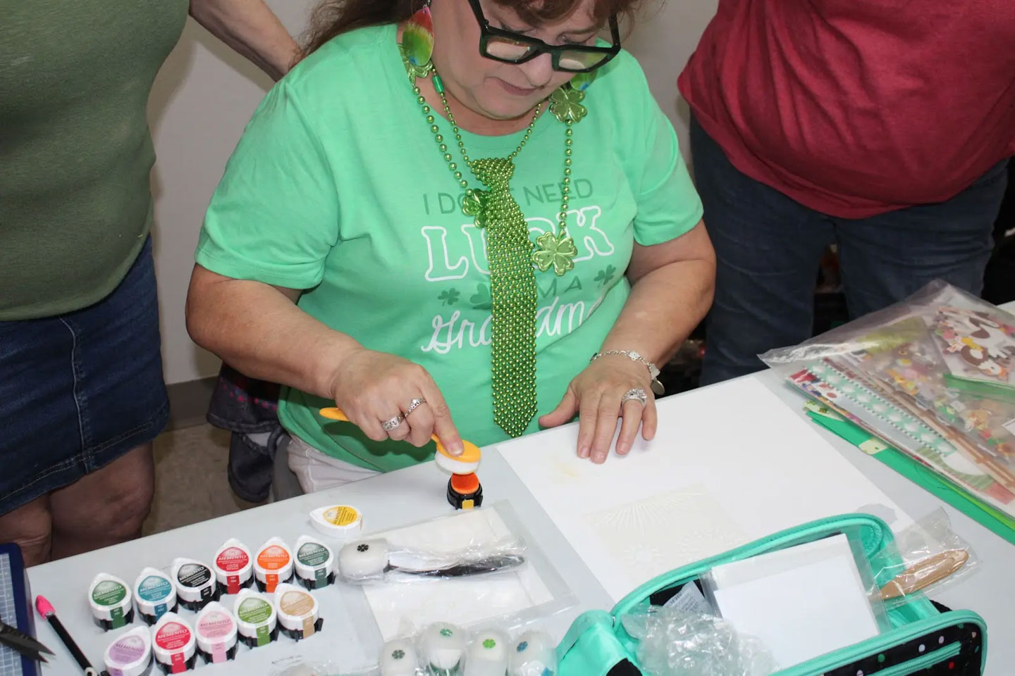Woman in green shirt with shamrock necklace using a sponge applicator on paper for a crafting project.